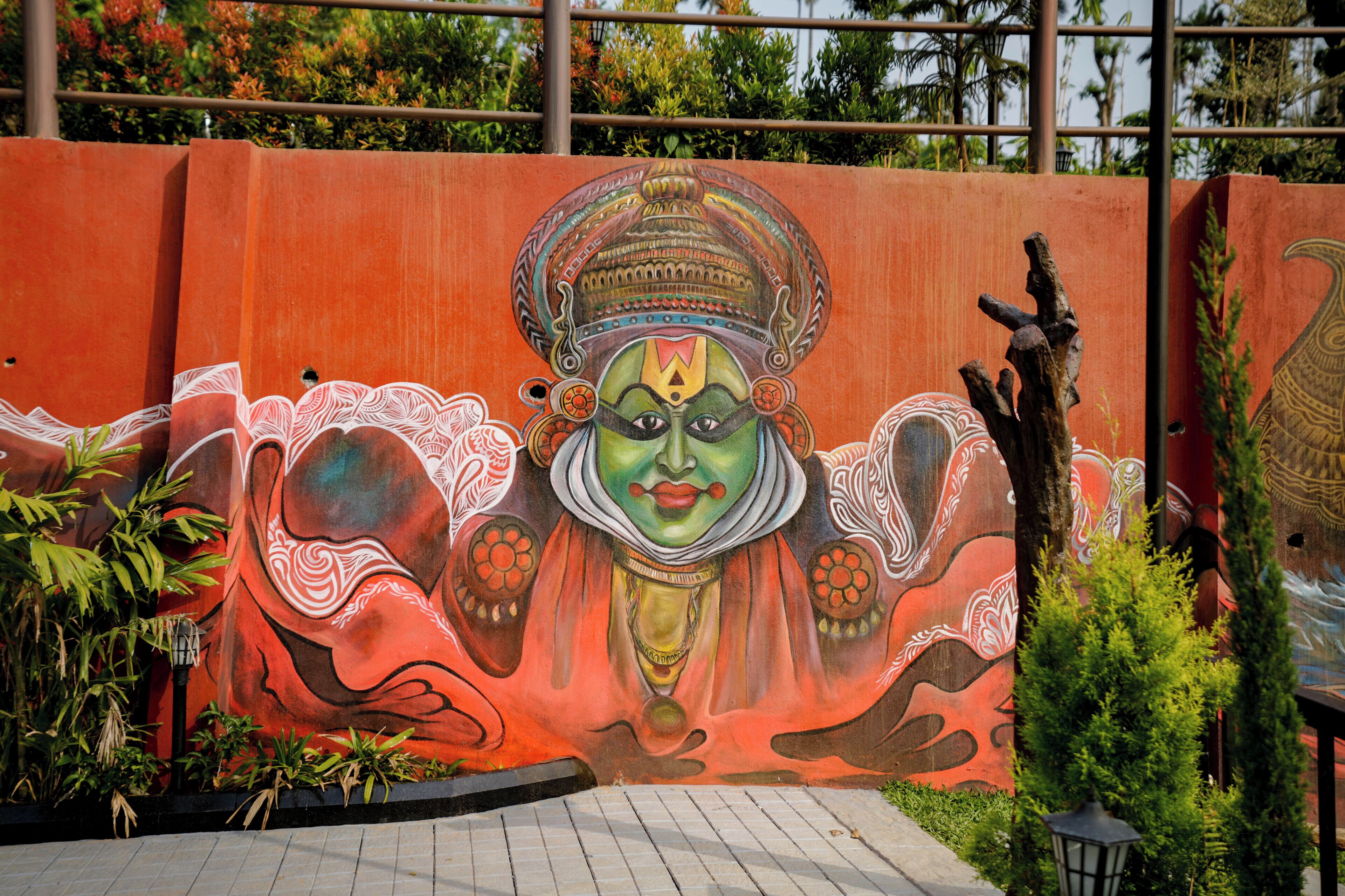 A mural of a deity with elaborate headdress and jewelry, set against a red wall with decorative patterns.