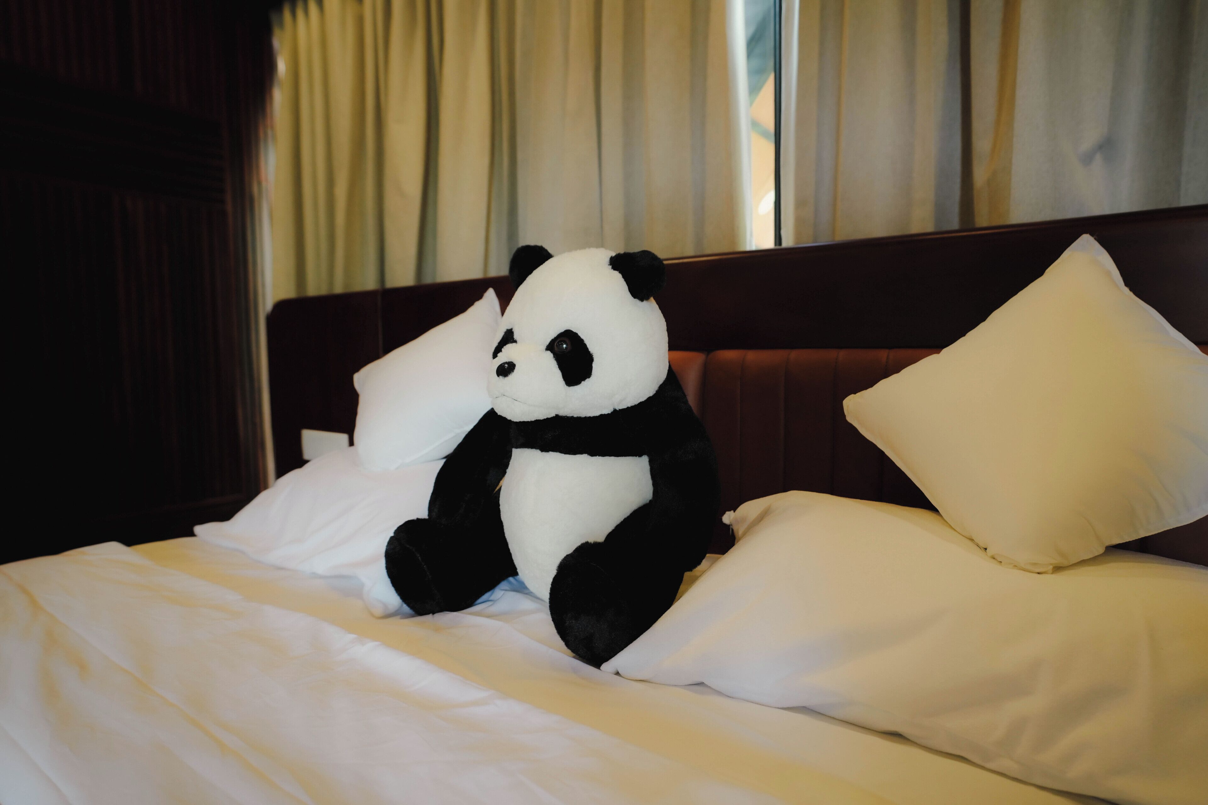 A bed with white bedding, a stuffed panda toy, and a wooden headboard.