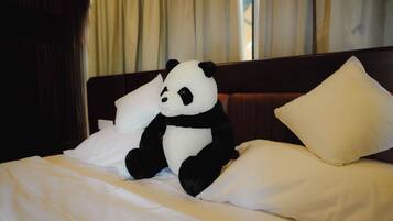 A bed with white bedding, a stuffed panda toy, and a wooden headboard.