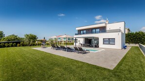 Een modern huis met twee verdiepingen, een zwembad, buitenzitplaatsen en een verzorgd gazon.