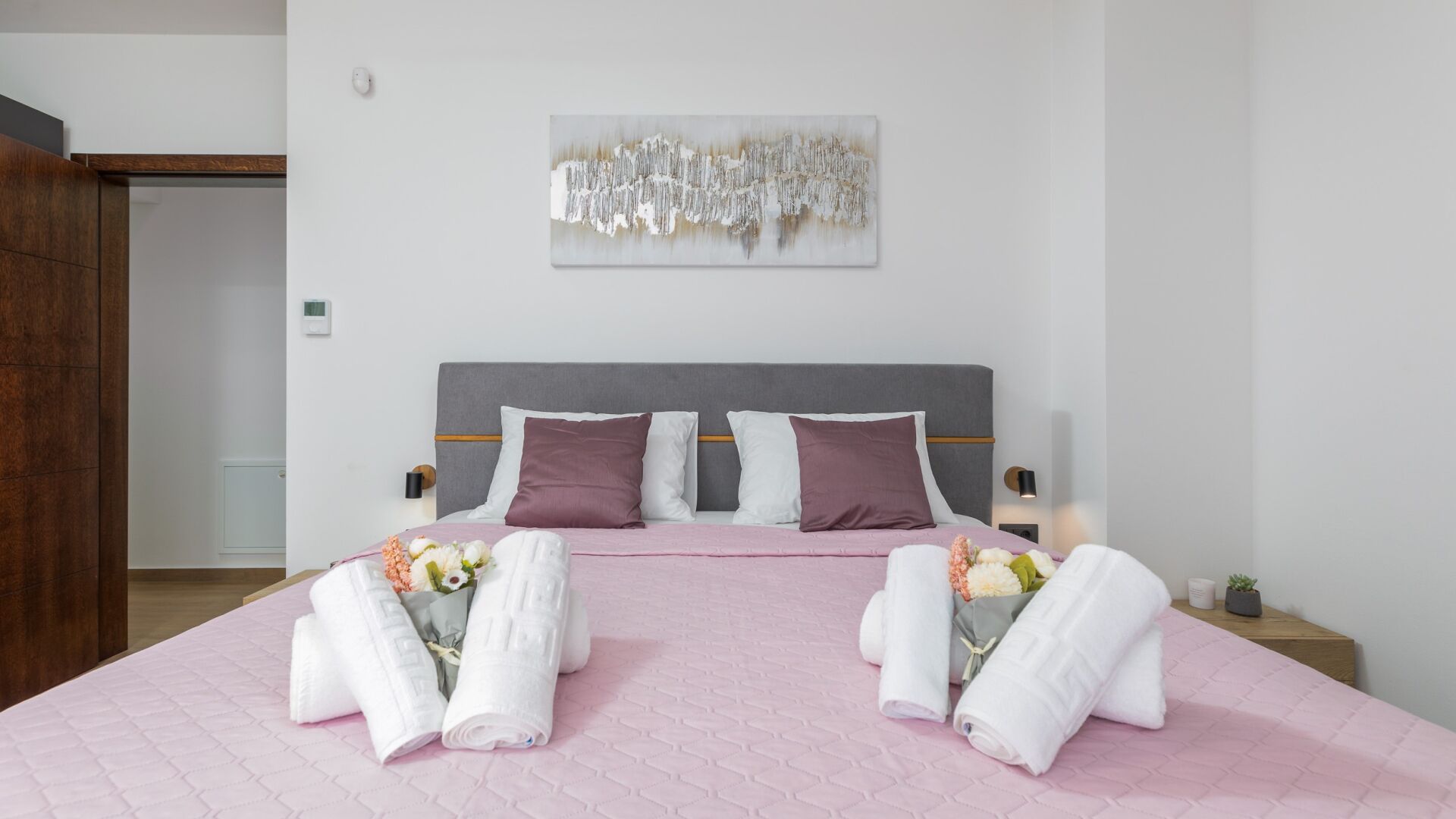 Un lit bien fait, avec une couverture rose, deux oreillers et des serviettes à motifs floraux.