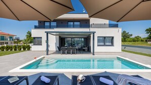Een modern huis met een zwembad, buiten zitplaatsen en een overdekt terras.