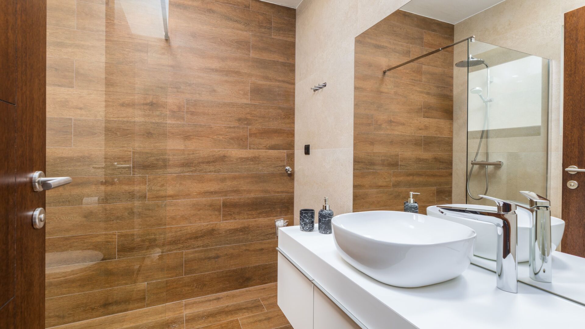 A modern bathroom with a large white sink, a glass shower enclosure, and wooden flooring.