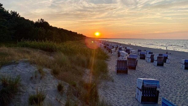Ein Strand mit Reihen von Liegestühlen und einem Sonnenuntergang im Hintergrund.