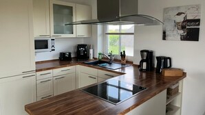 Eine moderne Küche mit weißen Schränken, einer Holz Arbeitsplatte, einem eingebauten Herd, einer Kaffeemaschine und einem Fenster, das natürliches Licht hereinlässt.