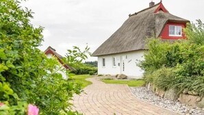 Ein Pfad führt zu einem traditionellen Haus mit einem Strohdach und weißen Wänden.