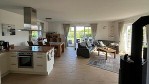 Eine moderne Küche mit Einbauofen, Essbereich mit Tisch und Stühlen, eine Couch und ein großes Fenster mit Vorhängen.