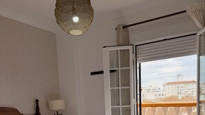 A hotel room with a bed, a lamp, a view of the city through a glass door, and a balcony with a railing. - Hotel Victoria Matalascañas (Matalascañas)