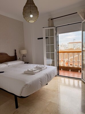 Quarto de hotel com uma cama, uma luminária, vista da cidade por uma porta de vidro e uma varanda com guarda-corrimão.