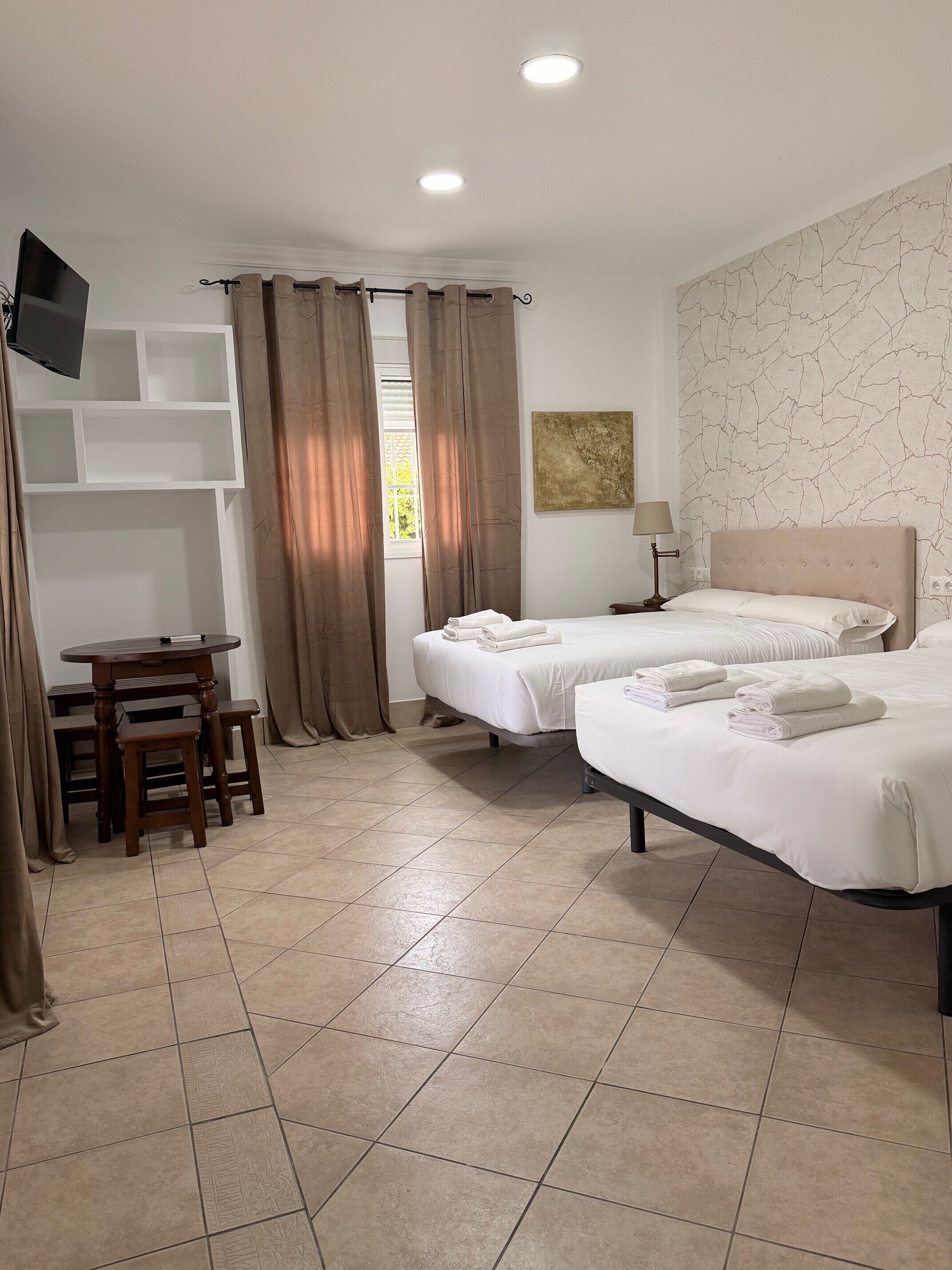Une chambre d’hôtel avec deux lits, un bureau, une télévision et une fenêtre avec des rideaux.