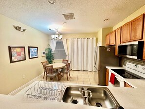 A kitchen with a stainless steel sink, a microwave, a refrigerator, wooden cabinets, and a dining area with a table and chairs.