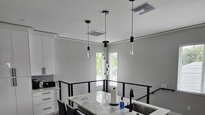 Una cocina moderna con una isla central, taburetes negros y luminarias colgantes.