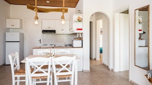 A kitchen with white cabinets, a wooden ceiling, and a dining area with white chairs. - Serenity Apartments (Corfu)
