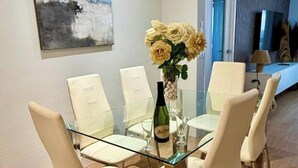 A dining area with a glass table, white chairs, a vase with flowers, and a bottle. - Front line beach - sea view - terrace (Fuengirola)