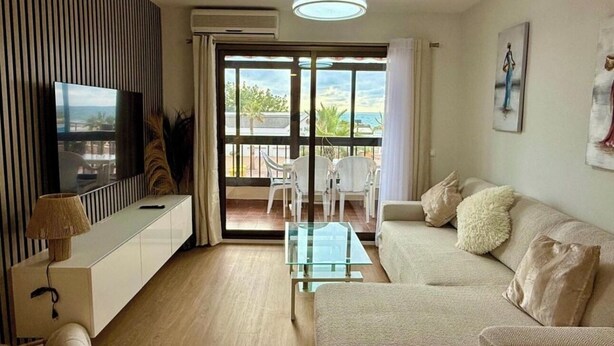 A modern living room with a sofa, a glass coffee table, a TV, and a balcony with chairs. - Front line beach - sea view - terrace (Fuengirola)