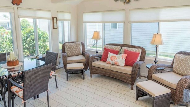 A sunlit room with wicker furniture, a glass table, and large windows.