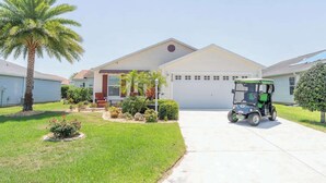 A residential building with a garage, a golf cart, and a well-maintained lawn with palm trees.