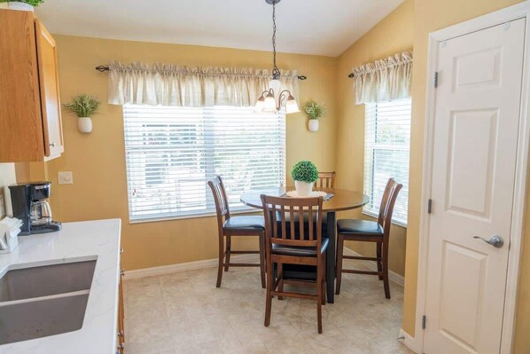 A dining area with a round table, four chairs, a coffee maker, and two potted plants.