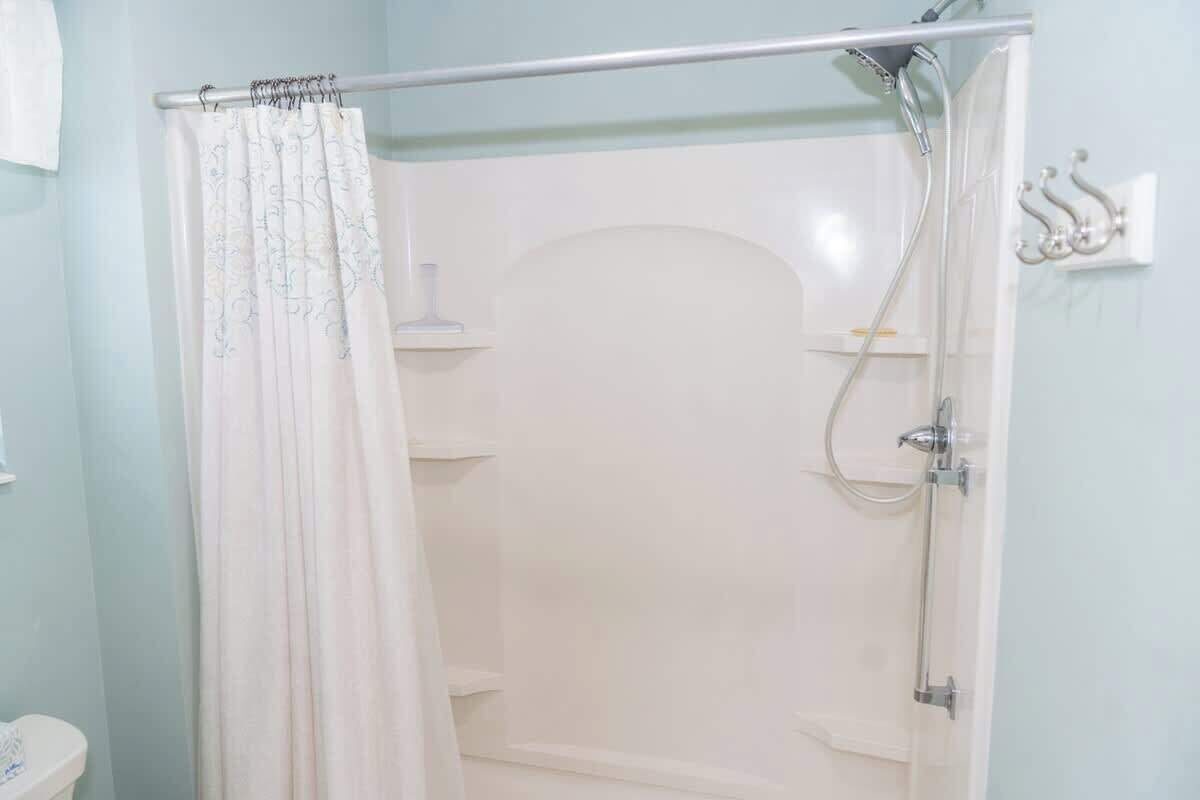 Un espace douche doté d’un rideau, d’une porte en verre et d’un pommeau de douche en métal.