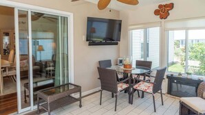 A patio area with a ceiling fan, a TV mounted on the wall, and a dining table with chairs.
