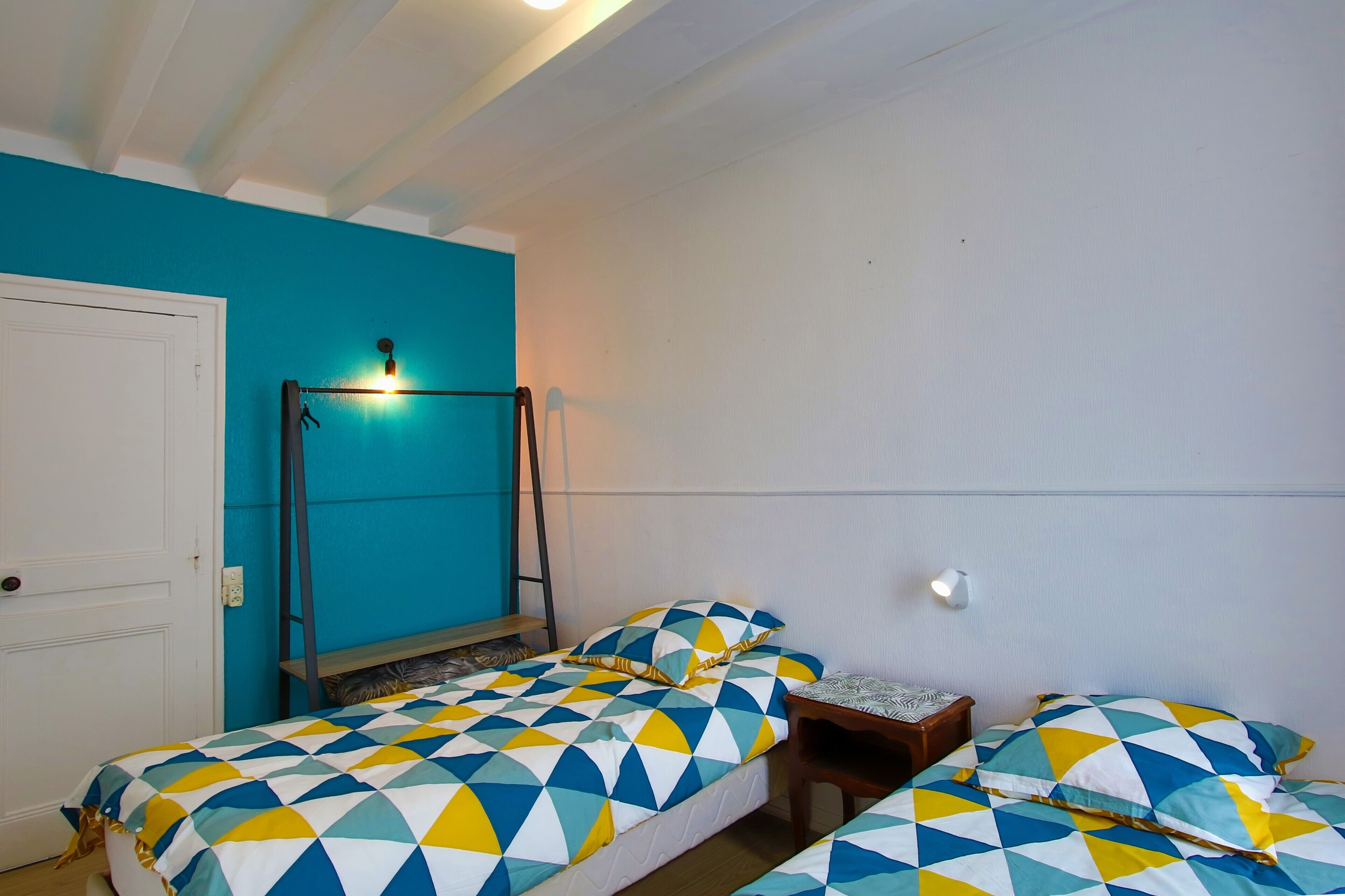 Une pièce avec deux lits, un banc, une porte et un luminaire fixé au mur.