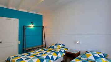 Une pièce avec deux lits, un banc, une porte et un luminaire fixé au mur.