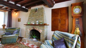 A cozy living room with a stone fireplace, two striped sofas, a wooden clock, and a window with curtains.