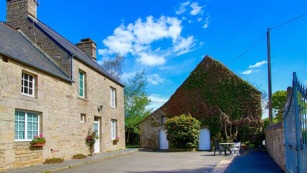 A stone building with a thatched roof, a paved street, and a gate.