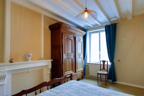 Une pièce comprenant un lit, une armoire en bois, une chaise, une fenêtre avec des rideaux et un luminaire suspendu.