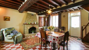 A cozy room with a fireplace, checkered floor, wooden beams, a dining table with chairs, and a sofa.