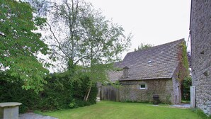 A stone building with a tiled roof, a grassy yard, and a wooden fence.