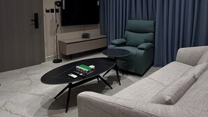 Un soggiorno moderno con televisore a schermo piatto, un divano grigio, un tavolino da caffè nero e una tenda blu.