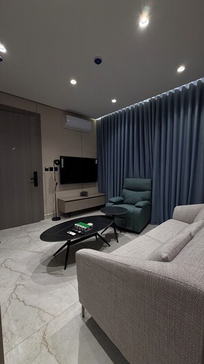 Ein modernes Wohnzimmer mit Flachbildfernseher, einem grauen Sofa, einem schwarzen Couchtisch und einem blauen Vorhang.