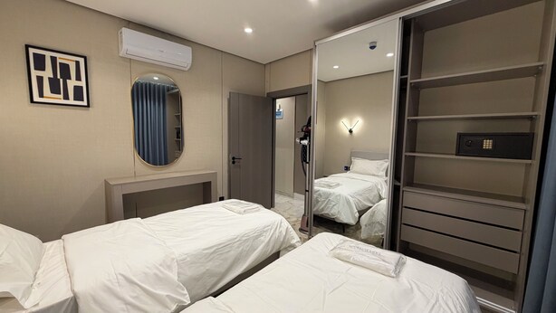 Camera d'albergo con due letti, un armadio, uno specchio e un condizionatore d'aria a soffitto.