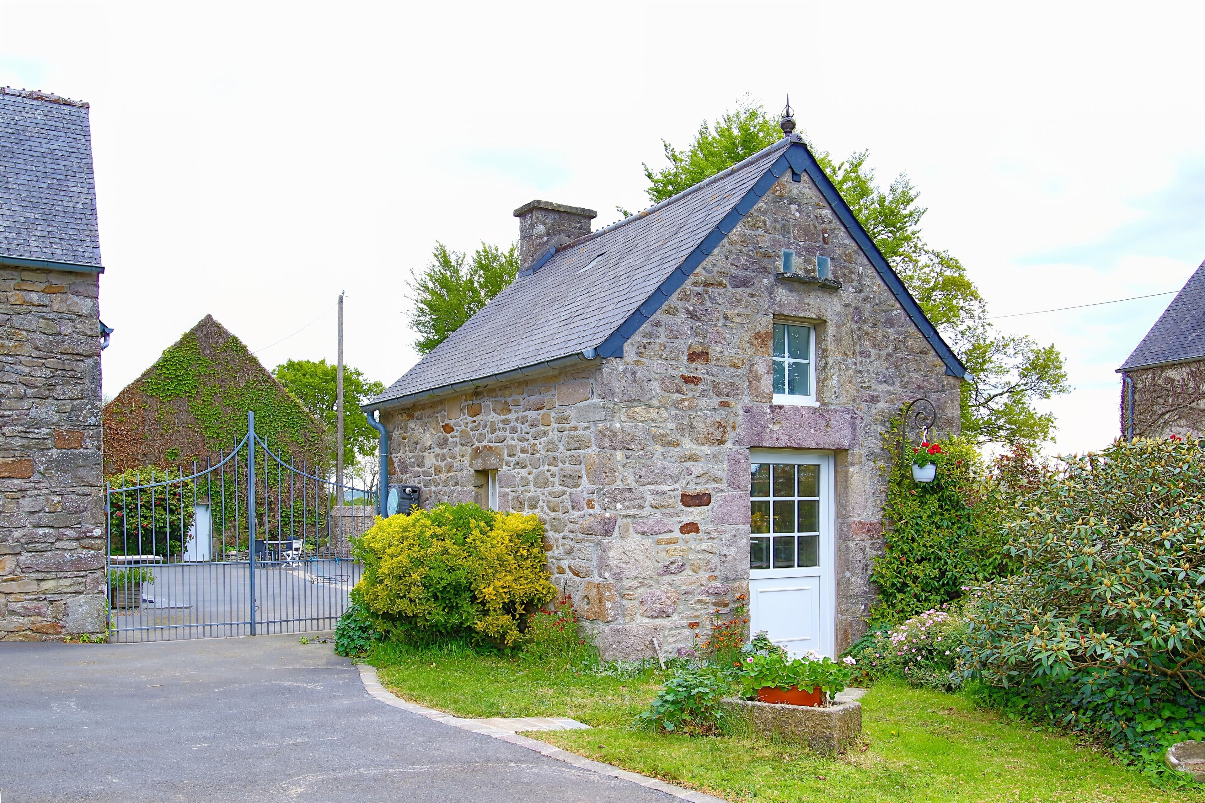 Une maison en pierre avec une porte blanche, entourée de verdure et dotée d’un portail en métal.