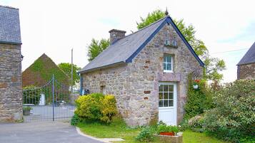 Une maison en pierre avec une porte blanche, entourée de verdure et dotée d’un portail en métal.
