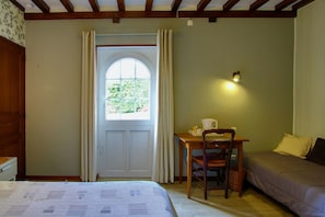 Una habitación con cama, una mesa con silla, una ventana con cortinas y una lámpara fijada a la pared.