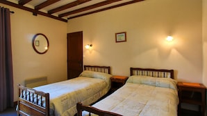 Una habitación con dos camas de madera, techo de madera con vigas a la vista, un espejo redondo y dos lámparas fijadas a la pared.