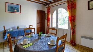 Comedor con una mesa redonda, sillas, mantel azul y una ventana con cortinas.