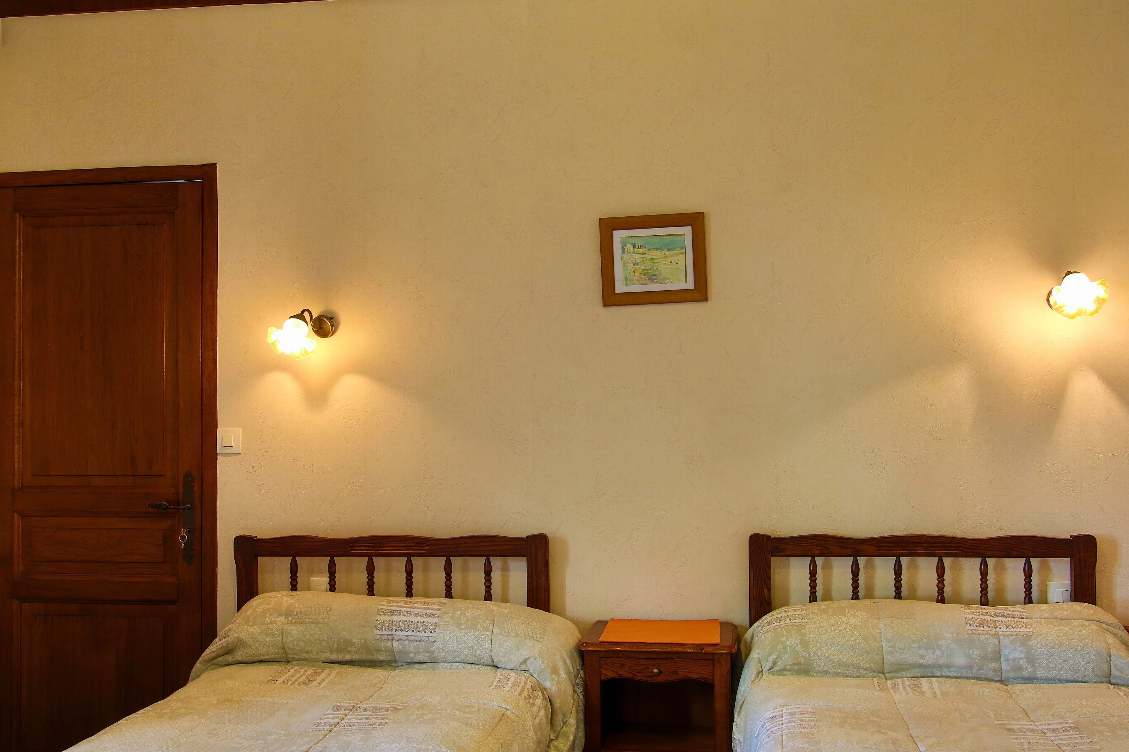 Une chambre avec deux lits, une porte en bois et des luminaires fixés au mur.