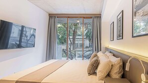 Ein Schlafzimmer mit Bett, Nachttisch, einem an der Wand befestigten Fernseher und einem Balkon mit Sitzgelegenheiten.