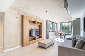 Ein modernes Wohnzimmer mit Flachbildfernseher, einer Couch, einem Essbereich und großen Fenstern.