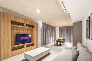 Un salon moderne doté d’un téléviseur à écran plat, d’étagères en bois, d’un canapé blanc et d’un coin repas avec une table et des chaises.