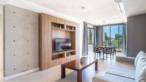 Un salon moderne doté d’un téléviseur, d’étagères en bois, d’un coin repas et d’un balcon avec vue.