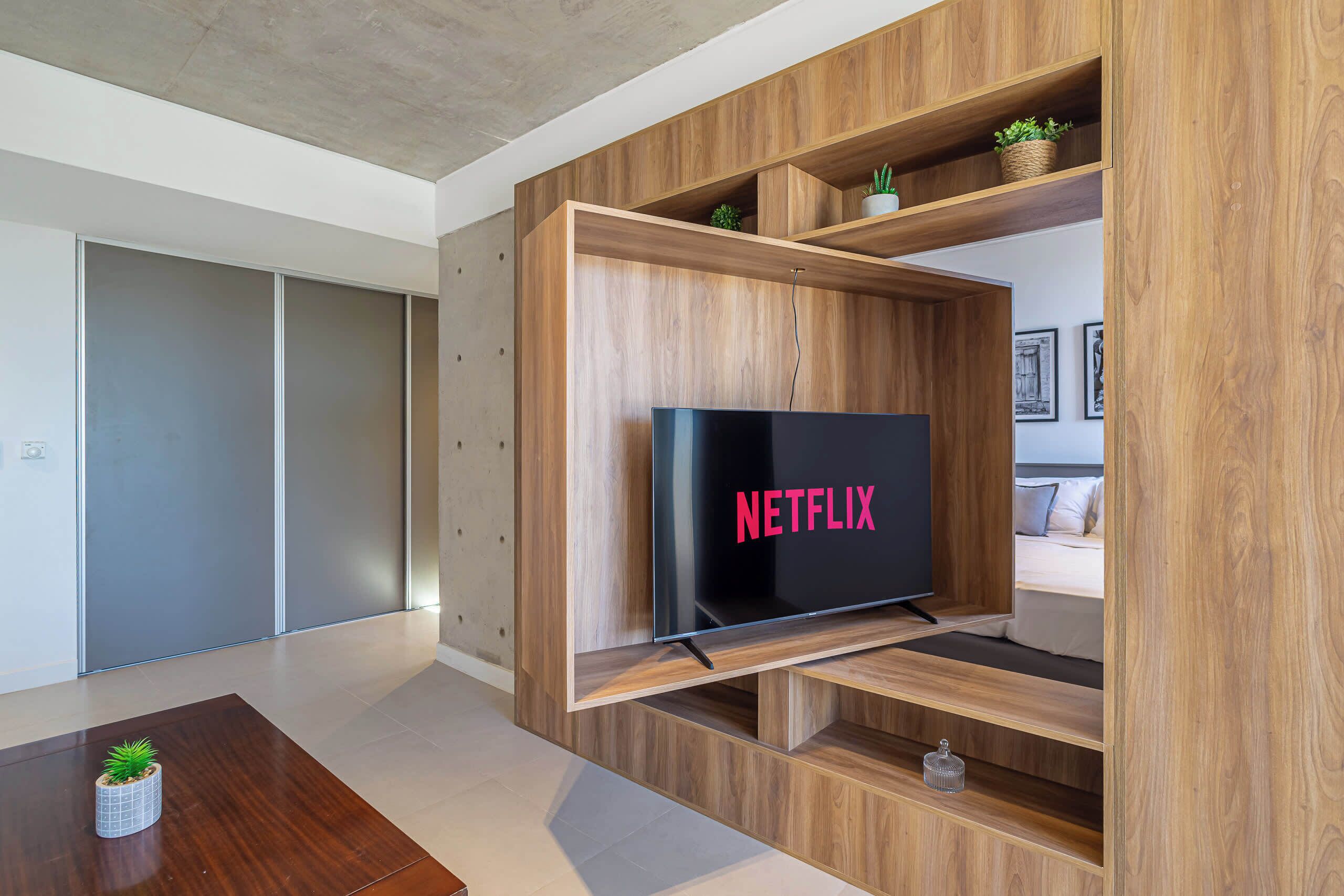 A modern living room with a wooden entertainment unit, a flat-screen TV, and a small table with a plant.
