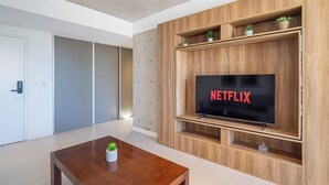 Un salon moderne avec un meuble TV en bois, un téléviseur à écran plat affichant le logo « NETFLIX », et une petite table sur laquelle est posée une plante.