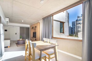 A modern living room with a dining table, chairs, a sofa, a TV, and a large window with a view of buildings. - Deluxe Apartment en Recoleta by Magno | 5A (Buenos Aires)