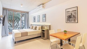 Ein modernes Hotelzimmer mit Bett, Esstisch und einem Balkon mit Blick auf Palmen.