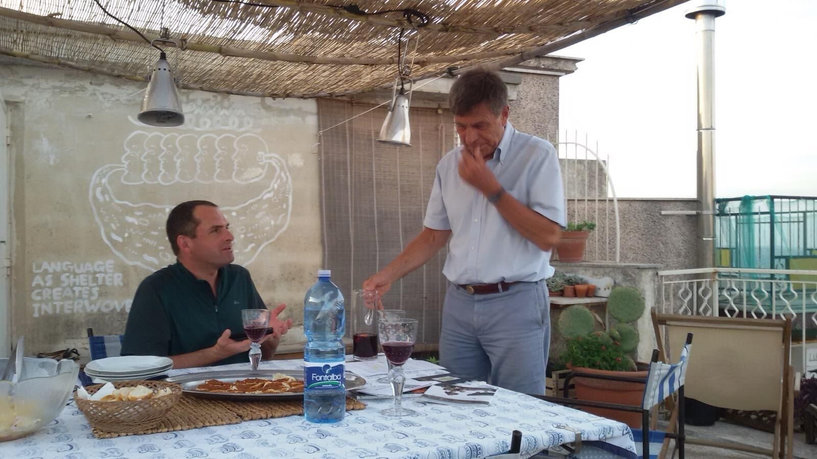 An outdoor dining area with a table set for two, a water bottle, and a bottle of red wine.