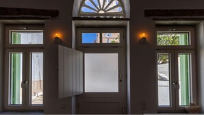 A door with a frosted glass panel, flanked by two windows with green shutters, and a decorative arch above. - Veggera Living, Tinos (Pyrgos)